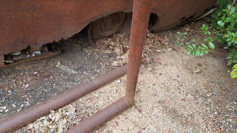 1973 Ford F-100 - A heavily rusted vehicle's side panel and tire are visible, resting on the ground amidst debris.