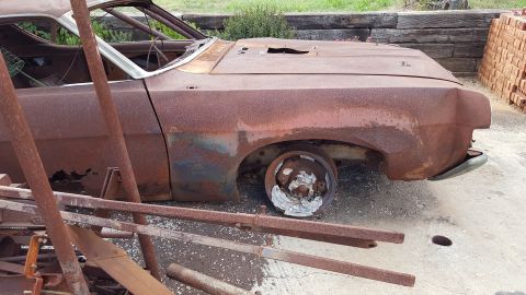 1973 Ford F-100 - A heavily rusted 1973 Ford Torino sits abandoned, missing its wheels and hood.