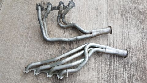 1973 Ford F-100 - Two exhaust manifolds are shown laid out on a concrete surface.