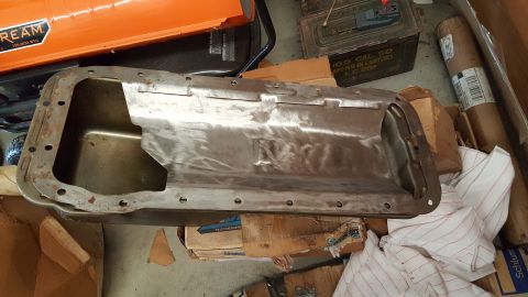 1973 Ford F-100 - A metal oil pan is shown in a workshop setting, resting on boxes and fabric.