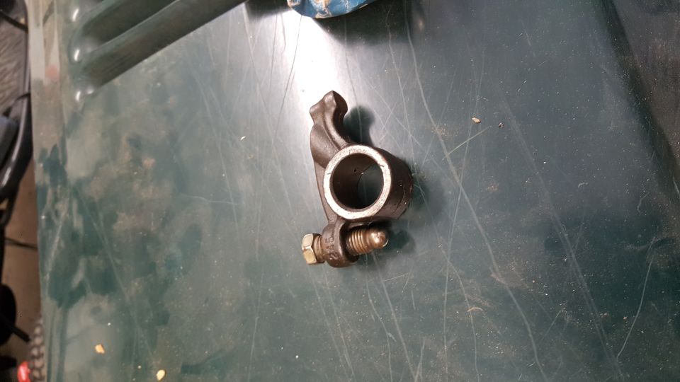 Engine valve rocker arm with bolt and nut on a green surface
