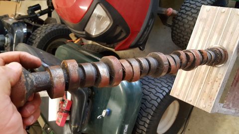 1973 Ford F-100 - A rusty camshaft is held up for inspection, with parts of lawnmowers visible in the background.
