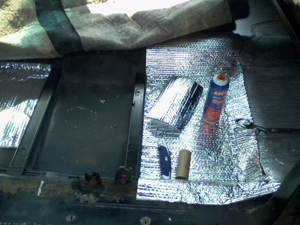 Car interior floor being lined with sound deadening material, utility knife, and adhesive spray