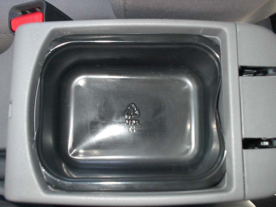 Empty black plastic bin in gray car center console, red seat belt buckle visible above