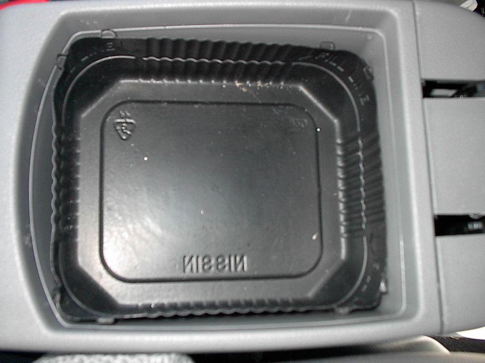 Black Nissin plastic food tray sitting inside a gray car console storage bin