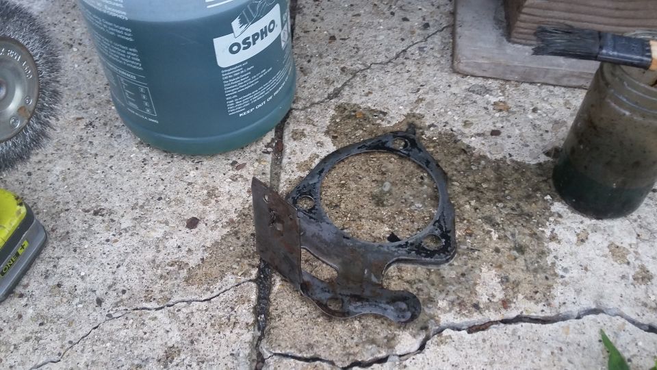 rusted metal part on cracked concrete next to a bottle of OSPHO and a brush in a jar