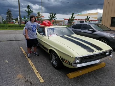 1971 Ford Mustang - A person poses with a yellow 1971 Ford Mustang Mach 1 dual black racing stripes.