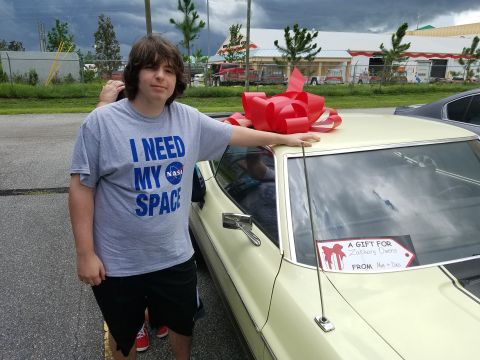 1971 Ford Mustang - A person stands next to a yellow coupe adorned with a large red bow, suggesting a gift.