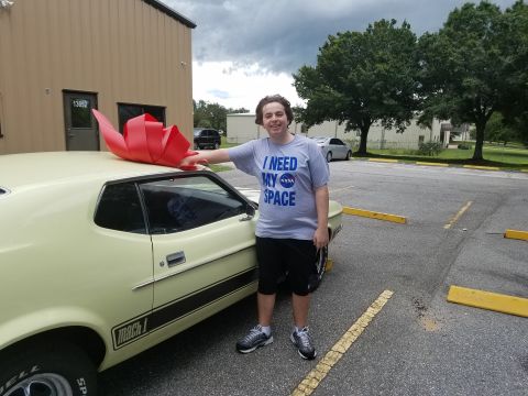 1971 Ford Mustang - A young man stands next to a pale yellow 1971 Ford Mustang Mach 1, which has a large red bow on its roof.