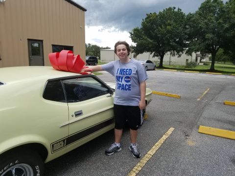 1971 Ford Mustang - A young man poses with a yellow 1971 Ford Mustang Mach 1, adorned with a large red bow, suggesting a special occasion.