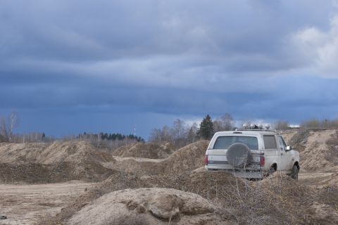 1993 Ford Bronco - A white 1993 Ford Bronco is seen from the rear, parked on a dirt terrain under a cloudy sky.