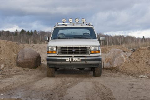 1993 Ford Bronco - Silver Ford Bronco with roof lights and off-road tires parked on a dirt road with large rocks and trees in the background.