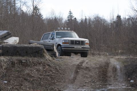 1993 Ford Bronco - A white Ford Bronco is parked on a dirt path surrounded by trees. The vehicle has a light bar on the roof.