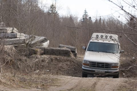 1993 Ford Bronco - White Ford F-Series truck with roof lights parked on a dirt path near concrete debris.