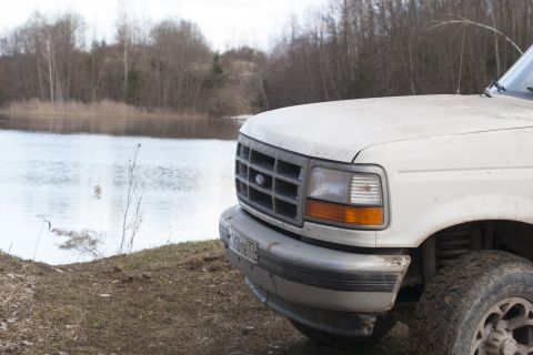 1993 Ford Bronco - A white 1993 Ford Bronco is parked by a lake, showing its front grille and headlight.