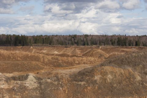 1993 Ford Bronco - A wide view of an open quarry with layered dirt formations and a treeline under a cloudy sky.