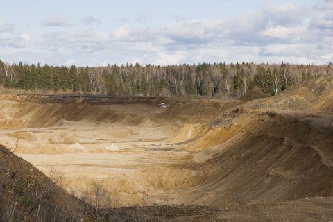 1993 Ford Bronco - A wide view of a quarry with layered dirt formations and a distant tree line under a partly cloudy sky.