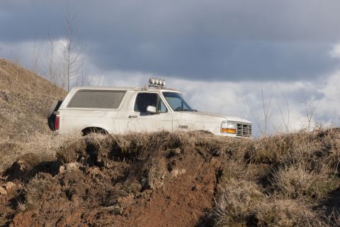 1993 Ford Bronco - This SUV is navigating a rough, muddy terrain under a cloudy sky.