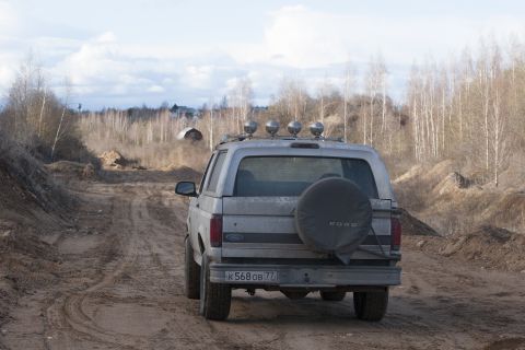 1993 Ford Bronco - A silver 1993 Ford Bronco is seen from the rear on a dirt road, equipped with a spare tire and roof lights.