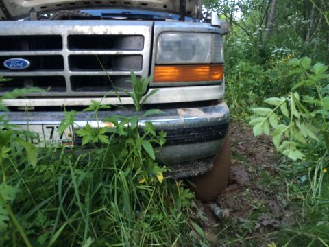 1993 Ford Bronco - Front end of a 1993 Ford Bronco is stuck in mud and overgrown vegetation.