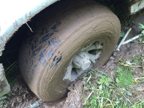 1993 Ford Bronco - A vehicle's tire is deeply embedded in mud and dirt, suggesting it is stuck off-road.