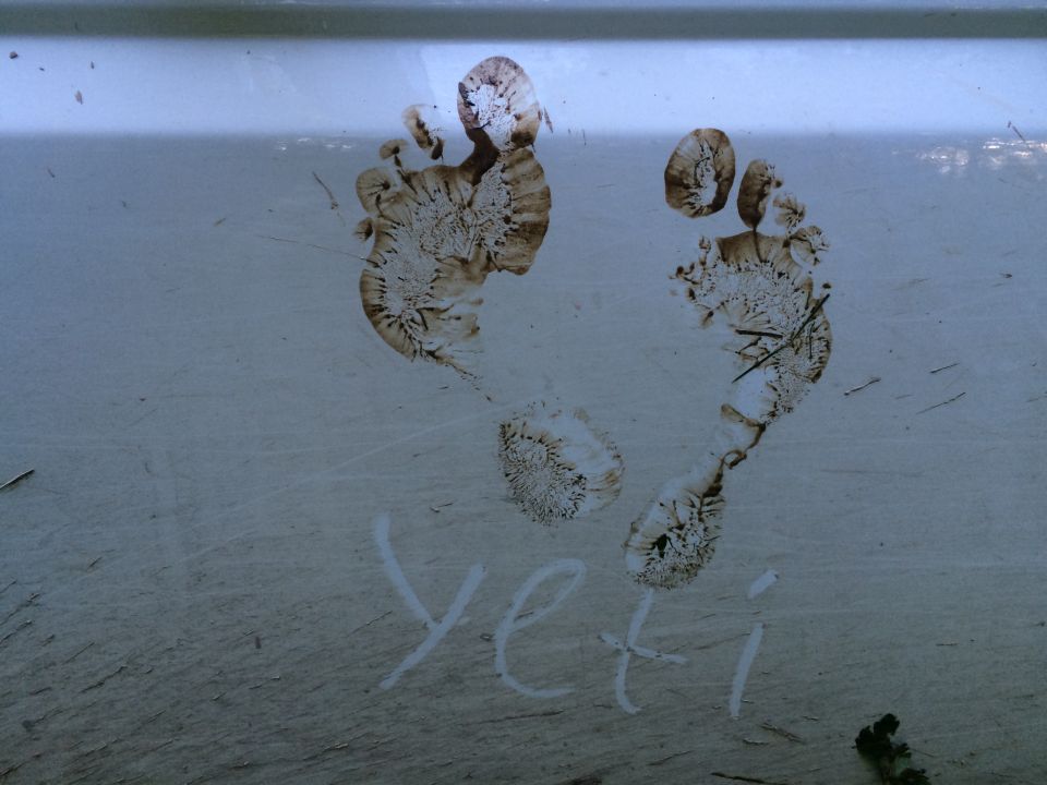 Muddy footprints and "yeti" written on a dirty vehicle surface