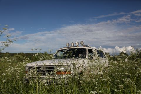 1993 Ford Bronco - A white SUV with auxiliary lights on the roof sits in a field of tall grass and white flowers under a cloudy blue sky.