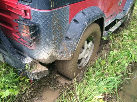 1993 Ford Bronco - This red Jeep Wrangler is stuck in the mud, with its rear tire deep in the muck.