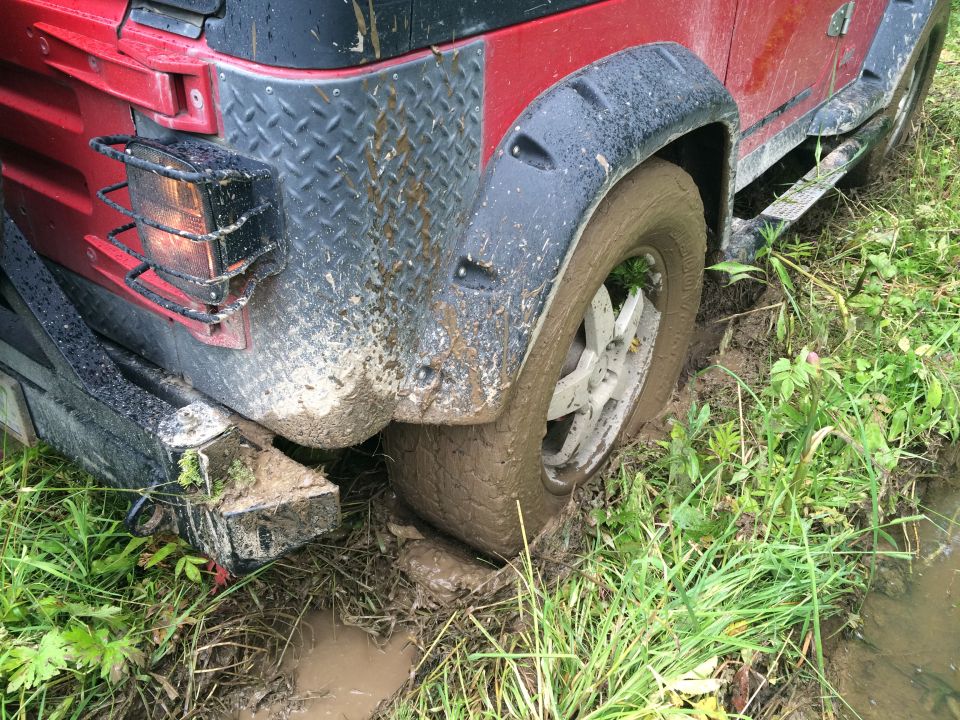 Red Jeep Wrangler's rear tire stuck in mud and grass
