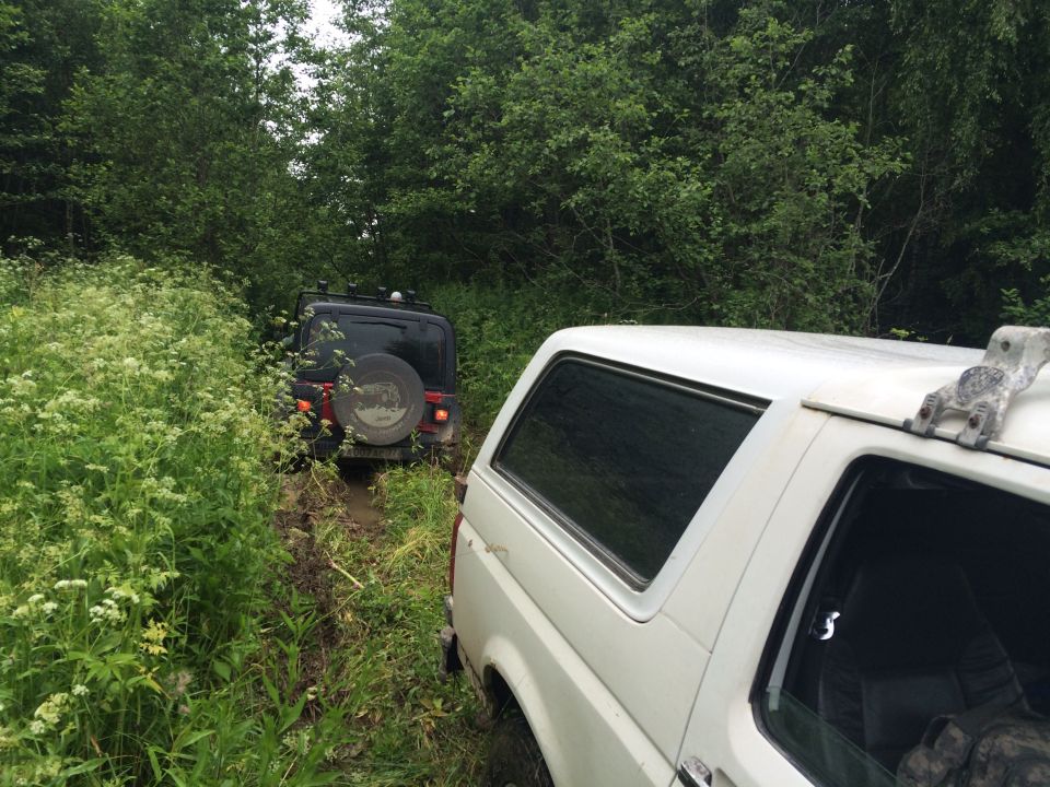 White SUV side view, black Jeep in muddy path behind it