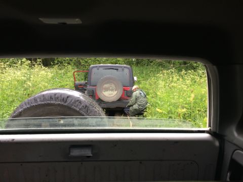 1993 Ford Bronco - Two Jeeps are seen off-road in a field, with one person attending to the rear of the red Jeep.