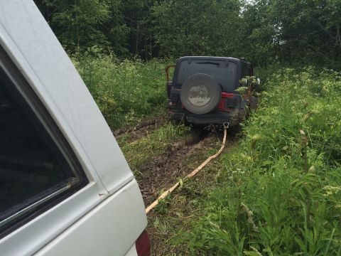 1993 Ford Bronco - A Jeep Wrangler is stuck in the mud, with a tow strap attached to another vehicle.