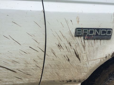1993 Ford Bronco - Mud covers the side of a 1993 Ford Bronco, obscuring the paint but not the BRONCO emblem.
