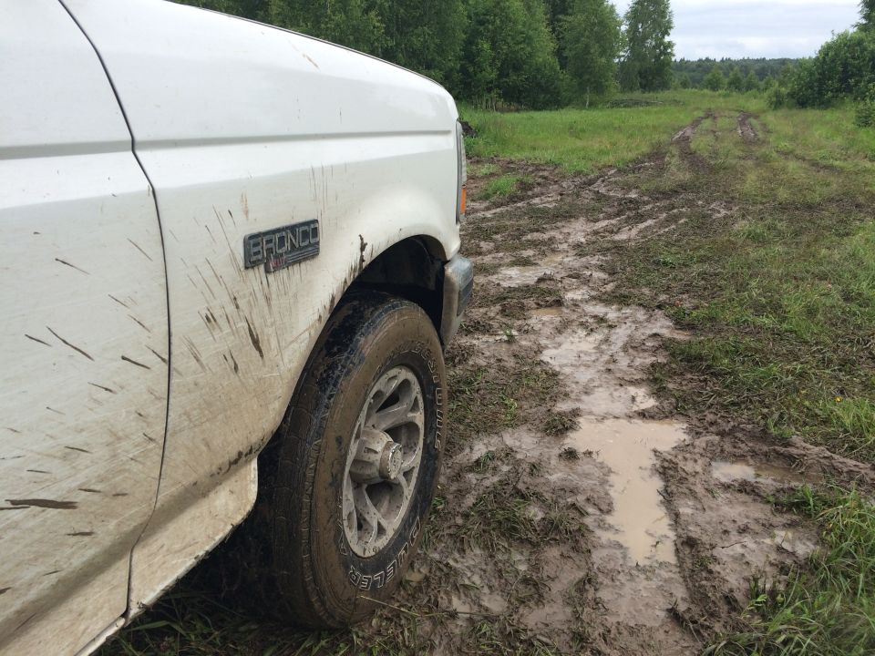 White 1993 Ford Bronco driving on a muddy dirt road