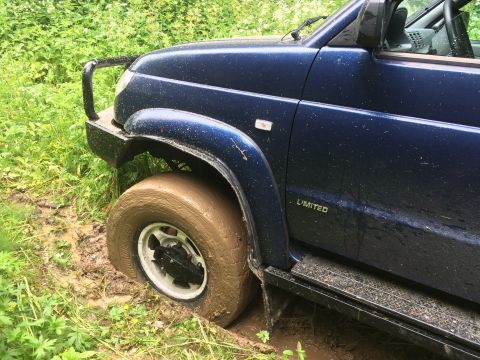 1993 Ford Bronco - A blue SUV is stuck in mud, with its front wheel submerged in the mire.