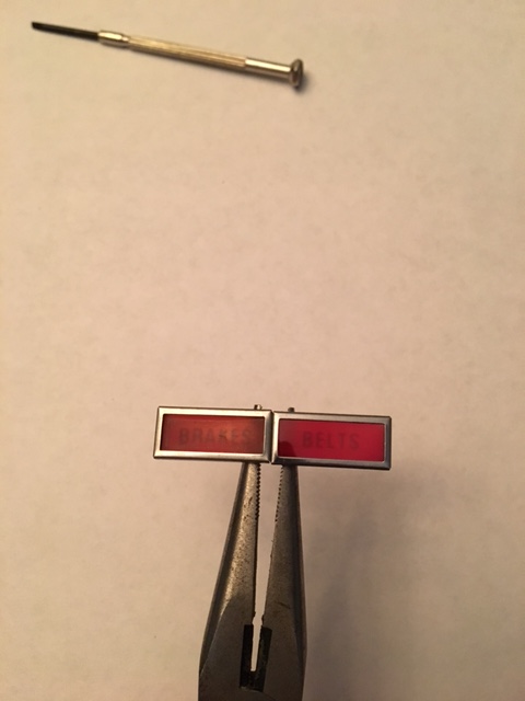 1968 Mercury Cougar - Pliers hold red warning light lenses for BRAKES and BELTS, with a small screwdriver nearby.