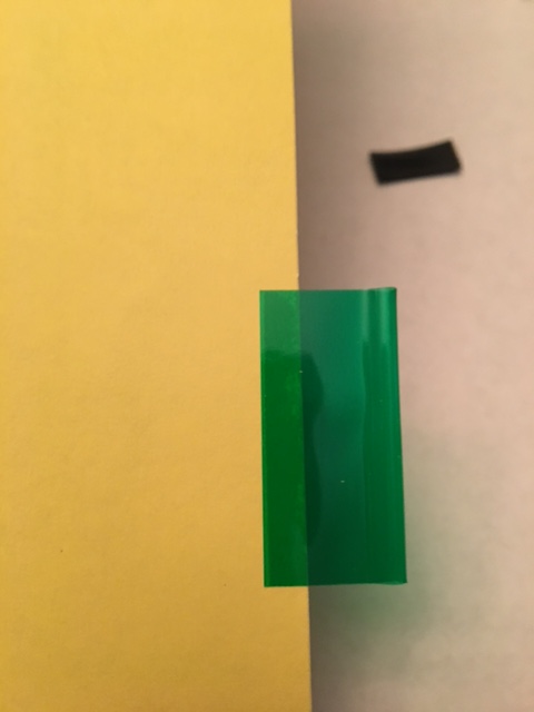 1968 Mercury Cougar - A green plastic strip is placed on a yellow surface, with a black piece of tape visible in the background.