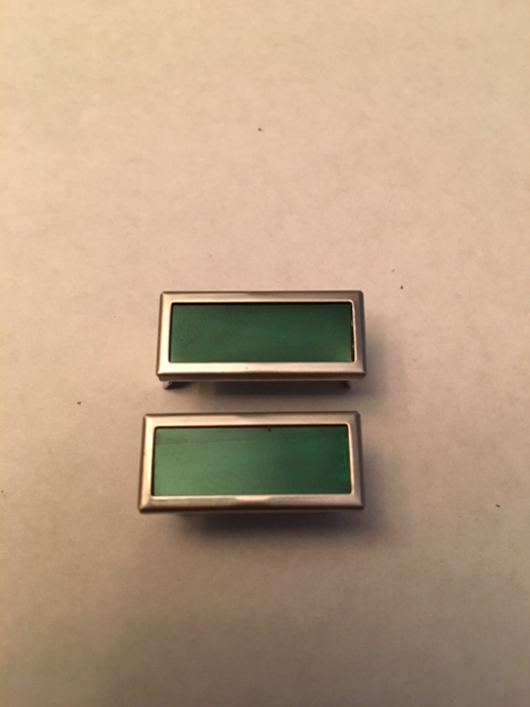 1968 Mercury Cougar - Two green emblems with chrome trim are shown against a neutral background.