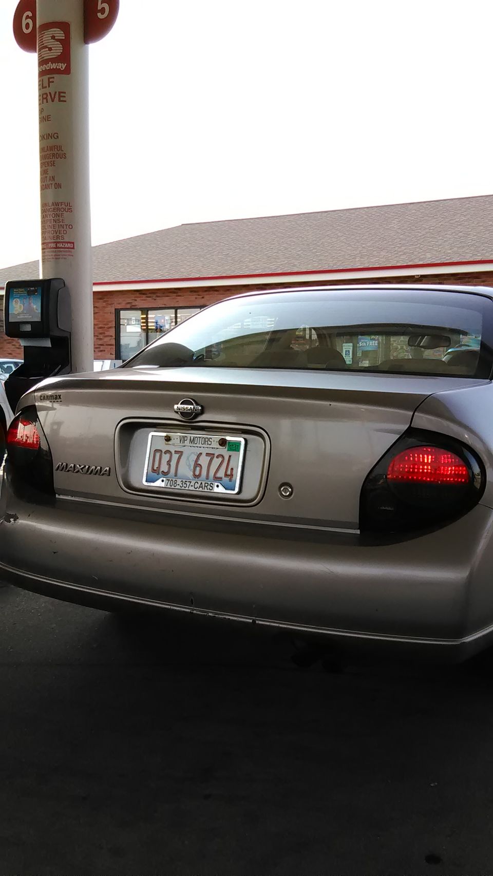 Rear view of a silver Nissan Maxima with tinted taillights at a Speedway gas pump