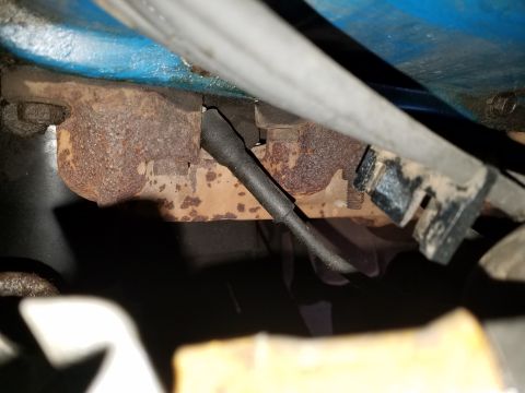 1971 Ford Mustang - A close-up view of a rusty exhaust manifold with a black wire, part of a vehicle's engine.