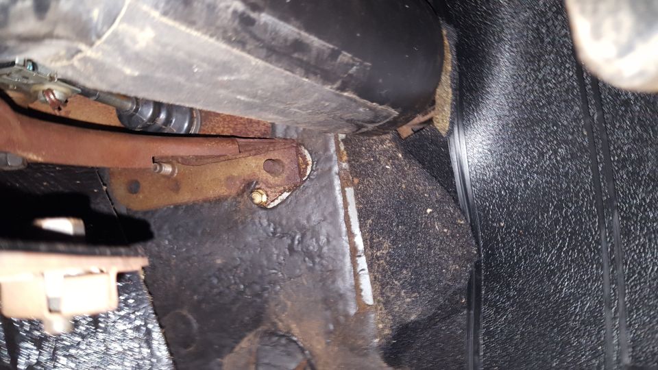 Close-up of rusty metal bracket and black carpet on a car's floor