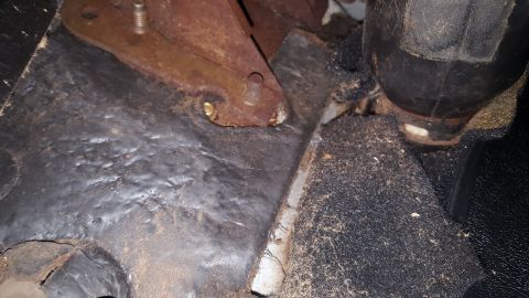 1971 Ford Mustang - The interior floor of a vehicle shows signs of wear and tear, with a rusty metal bracket and a black rubber pedal visible.