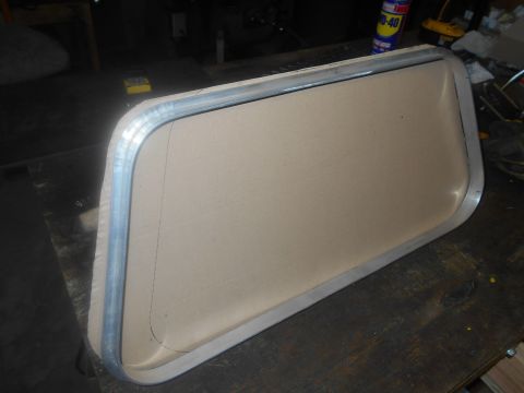 1992 Ford Bronco - A metal-framed window insert sits on a wooden surface, possibly for an RV or camper.