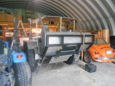 1992 Ford Bronco - An orange Volkswagen Beetle is parked in a garage, its rear end visible beside a large, unfinished custom vehicle.