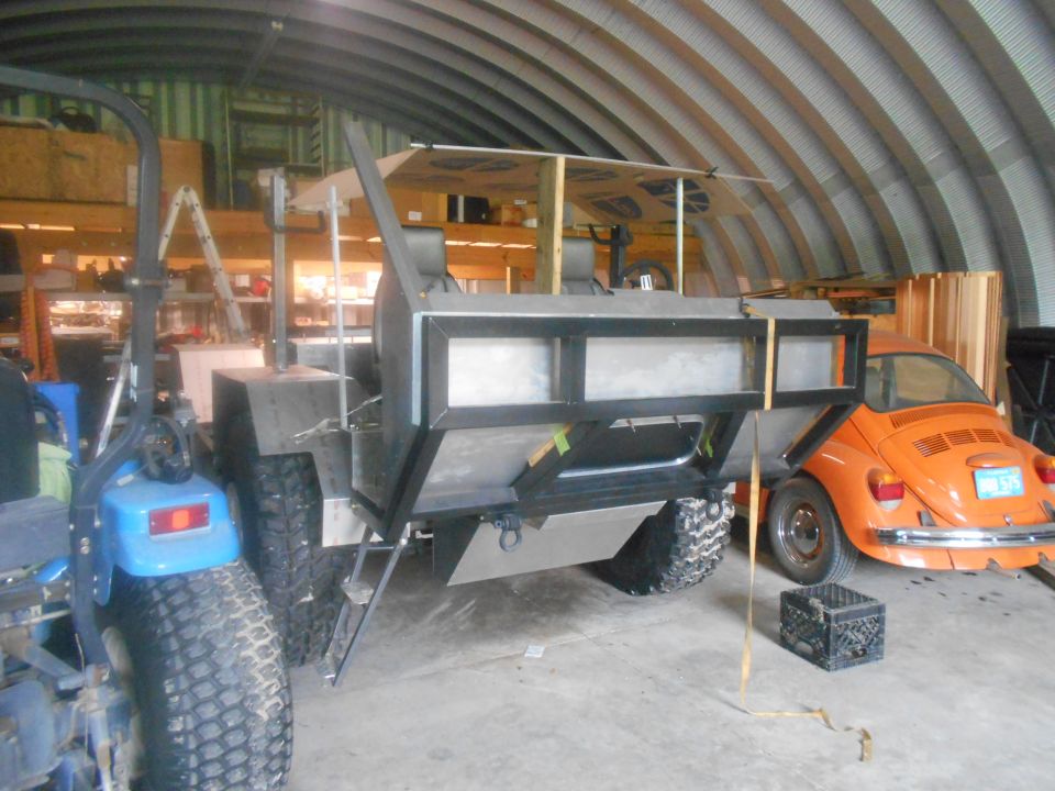 Orange Volkswagen Beetle, rear view, parked in a garage next to a custom-built vehicle