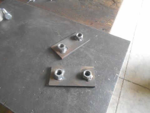 1992 Ford Bronco - Two metal plates with welded nuts sit on a larger metal surface, possibly for a project or repair.