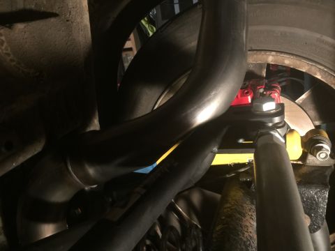 1983 Ford Mustang - Close-up view of exhaust pipes and suspension parts, including a red brake caliper and yellow bushings.