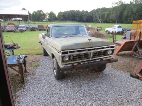 1967 Ford F-250 - A weathered green Ford F-Series truck sits in a rural yard with other vehicles and farm equipment.