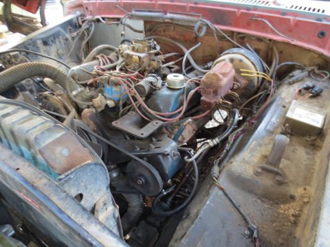 1967 Ford F-250 - The engine bay of a red truck displays a V8 engine with various components, including a carburetor and brake booster.