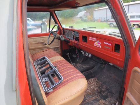 1967 Ford F-250 - Interior view of a red truck cab with a striped bench seat and a dashboard adorned with stickers.